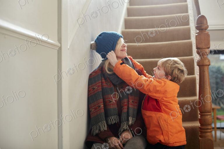 A boy pulling a hat over his mother's eyes.