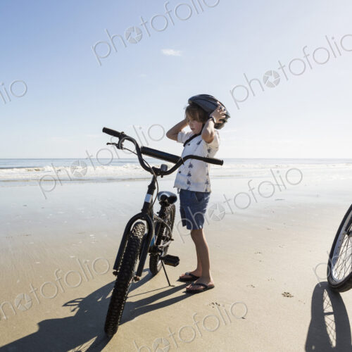 A boy putting on a cycle helmet on the beach, St. Simon's Island, Georgia
