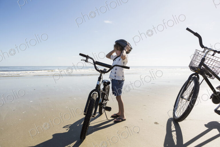 A boy putting on a cycle helmet on the beach, St. Simon's Island, Georgia
