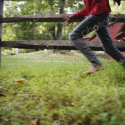 A boy running around a paddock fence outdoors. A boy running around a paddock fence outdoors.