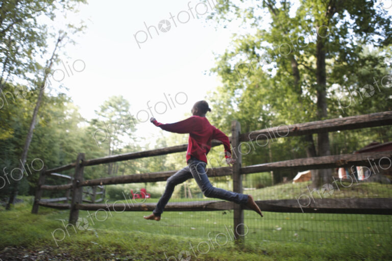 A boy running around a paddock fence outdoors.