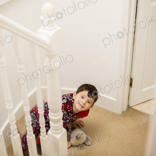 A boy sitting on the stairs, looking upwards and grinning.