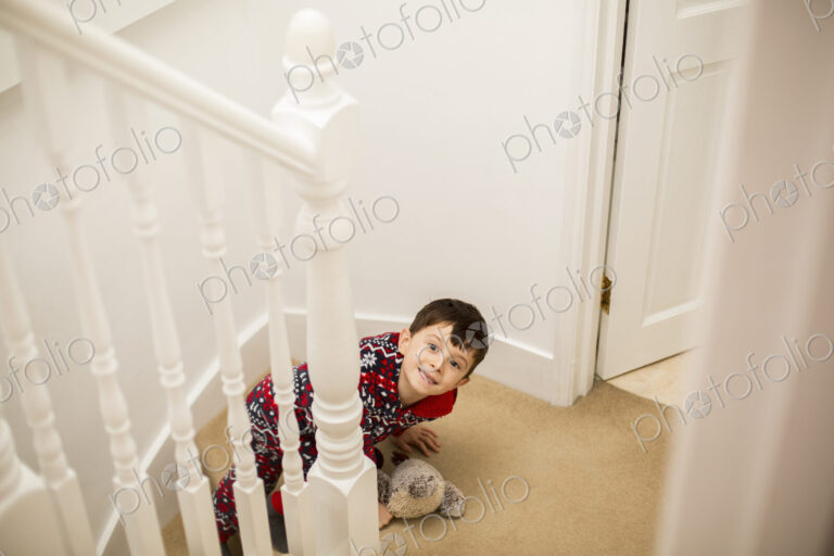 A boy sitting on the stairs, looking upwards and grinning.