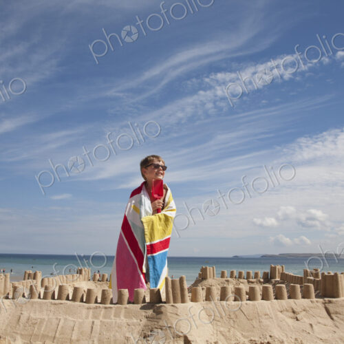 A boy standing beside a sandcastle, on top of a mound of sand. Beach. A boy standing beside a sandcastle, on top of a mound of sand. Beach.