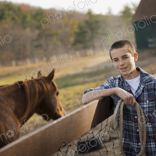 A boy standing by the fence of a horse paddock. A bay horse. A boy standing by the fence of a horse paddock. A bay horse.
