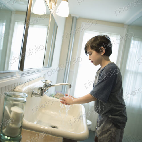 A boy standing in the bathroom, washing his hands under the tap. A boy standing in the bathroom, washing his hands under the tap.