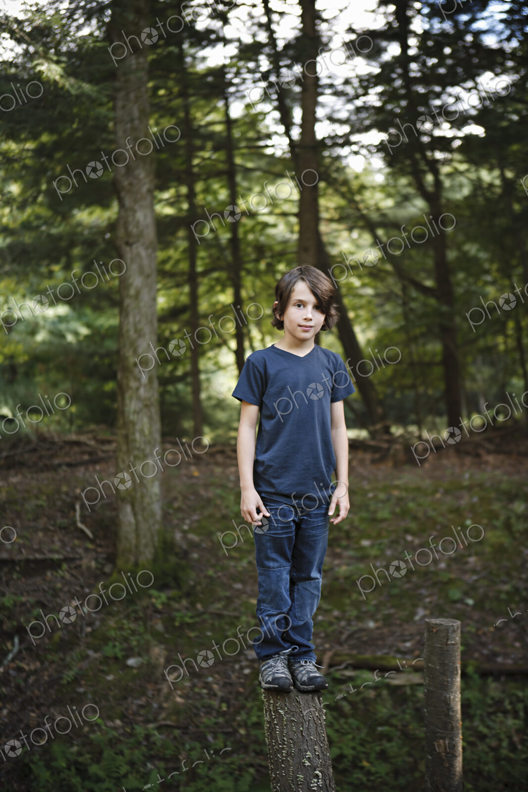 A boy standing on a narrow tree trunk, balancing and walking the plank.