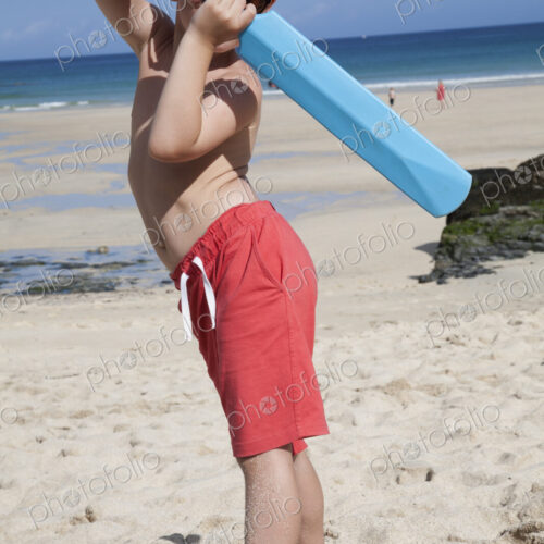 A boy standing on the sand with a small blue cricket bat in his hands. A boy standing on the sand with a small blue cricket bat in his hands.