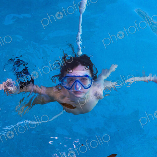 A boy swimming underwater in a pool with goggles.