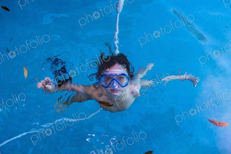 A boy swimming underwater in a pool with goggles.