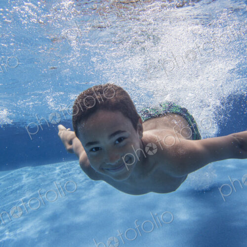A boy swimming underwater smiling at the camera. A boy swimming underwater smiling at the camera.