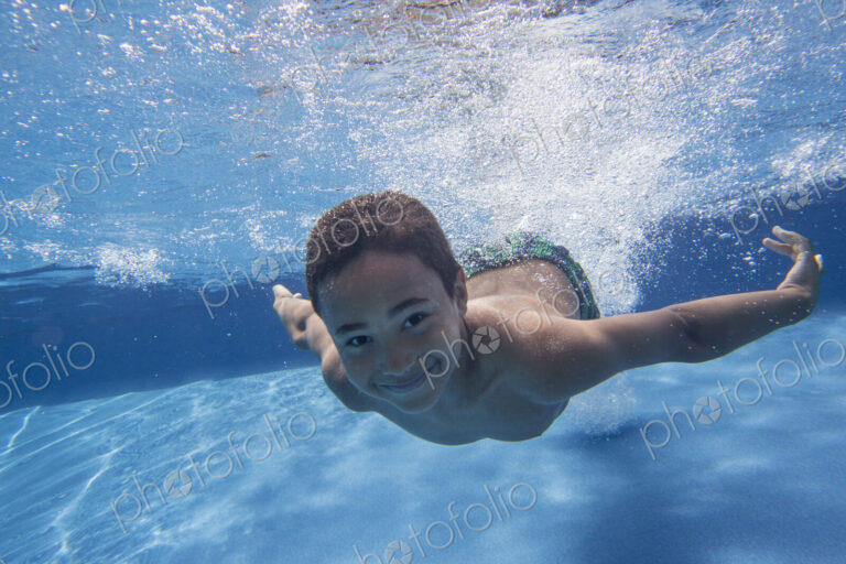 A boy swimming underwater smiling at the camera.