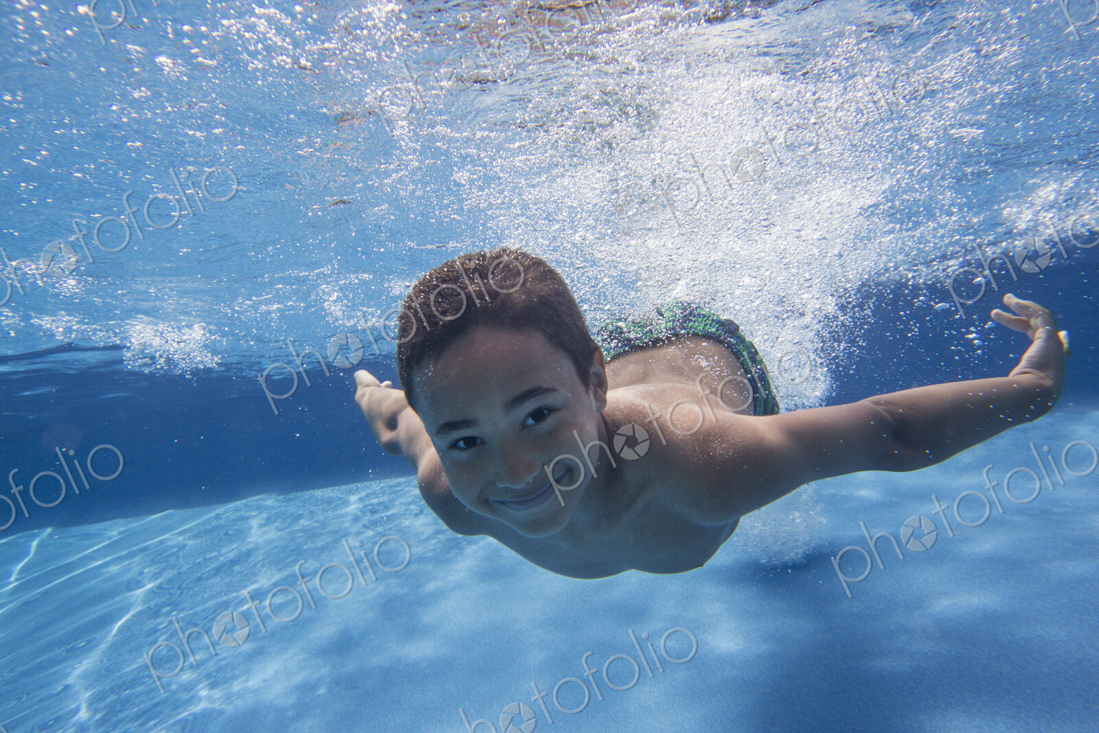 A boy swimming underwater smiling at the camera.