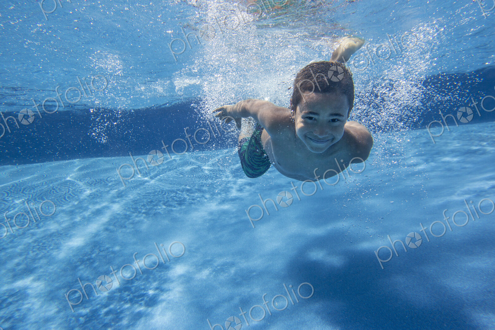 A boy swimming underwater smiling at the camera.