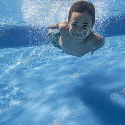 A boy swimming underwater smiling at the camera. A boy swimming underwater smiling at the camera.