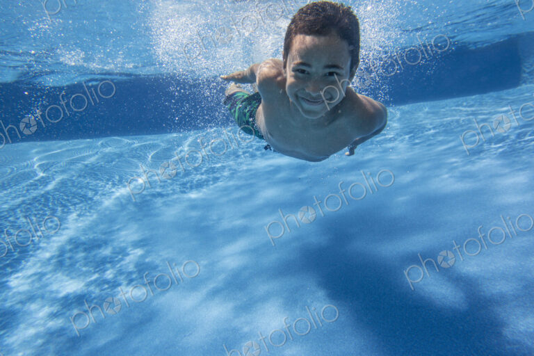 A boy swimming underwater smiling at the camera.