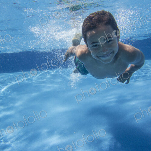 A boy swimming underwater smiling at the camera. A boy swimming underwater smiling at the camera.