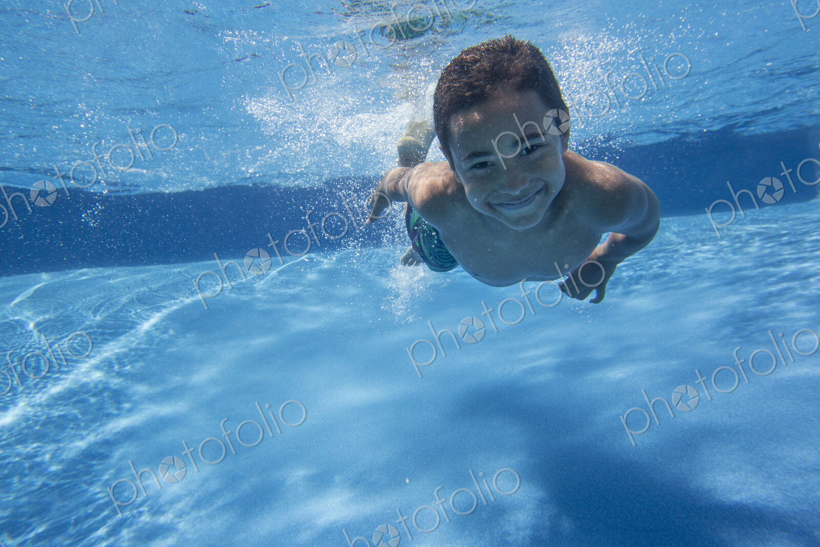 A boy swimming underwater smiling at the camera.