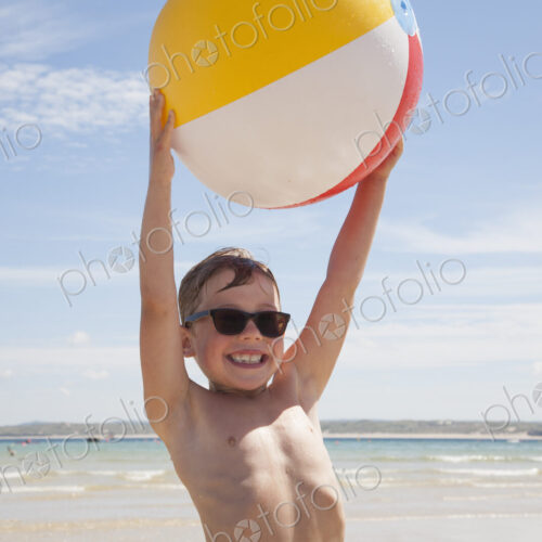 A boy wearing sunglasses on the beach. Holding an inflatable beach ball above his head. A boy wearing sunglasses on the beach. Holding an inflatable beach ball above his head.