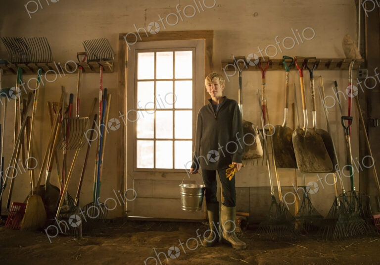 A boy with a feed bucket in the stables feedroom or toolshed of an animal sanctuary.…