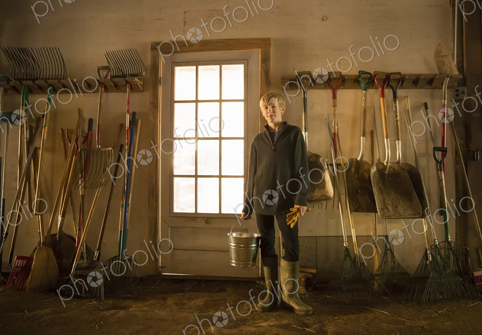 A boy with a feed bucket in the stables feedroom or toolshed of an animal sanctuary.…