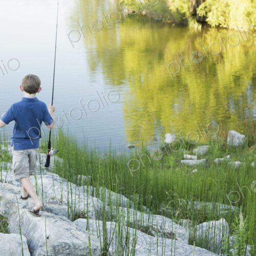 A boy with his fishing rod on the shore of a lake or river.