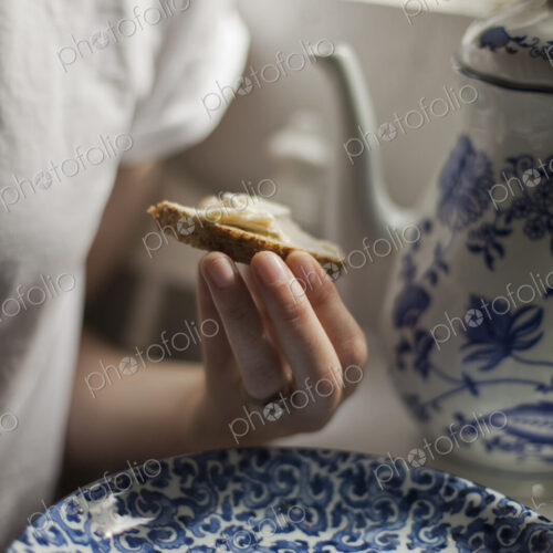 A breakfast table with a tall coffeepot and blue and white china plate. A woman…