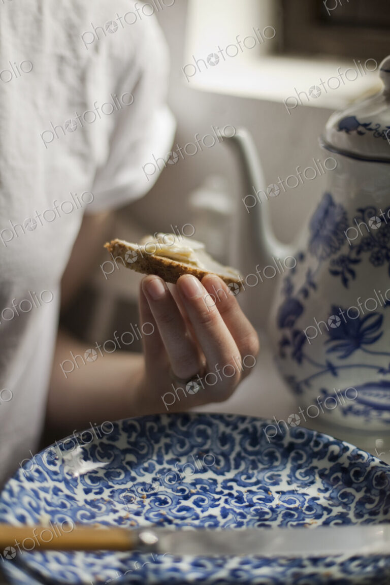 A breakfast table with a tall coffeepot and blue and white china plate. A woman…