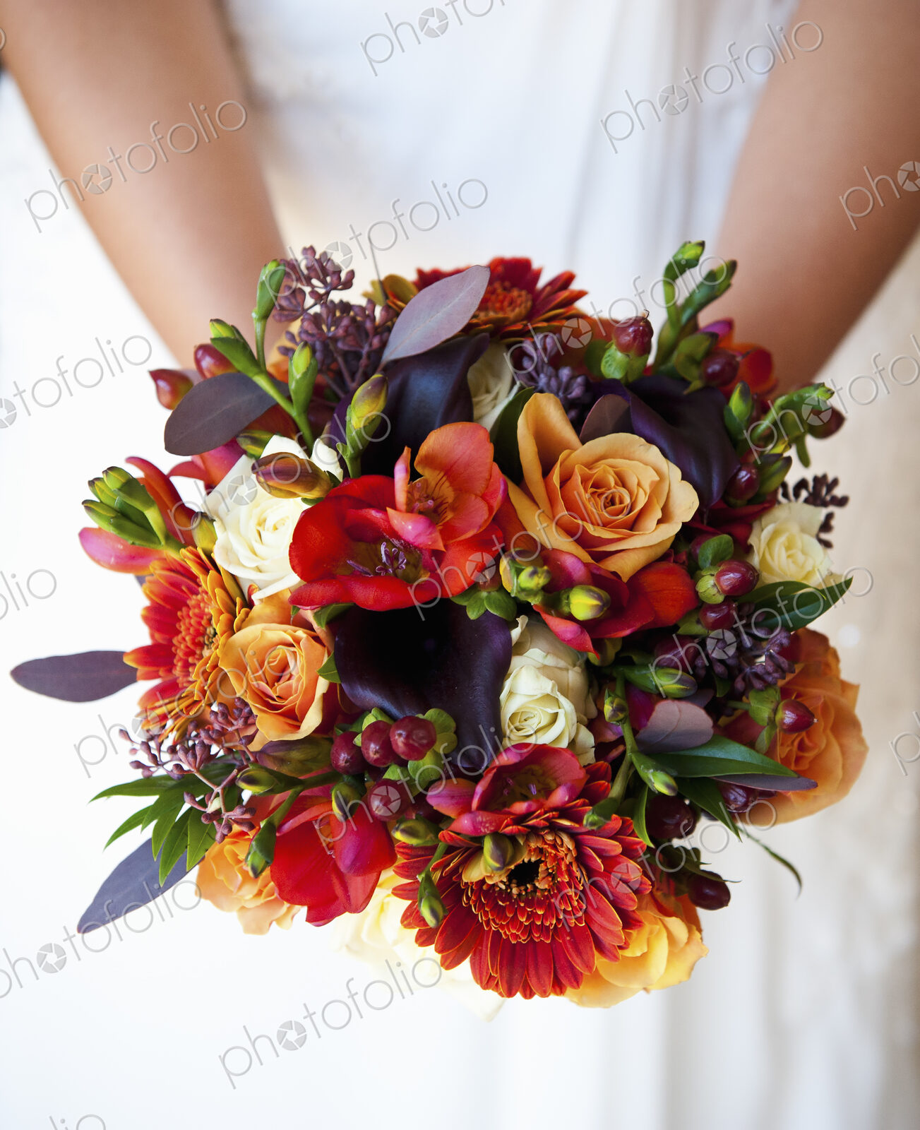 A bride holding a bridal bouquet of colourful red and orange flowers with purple toned…