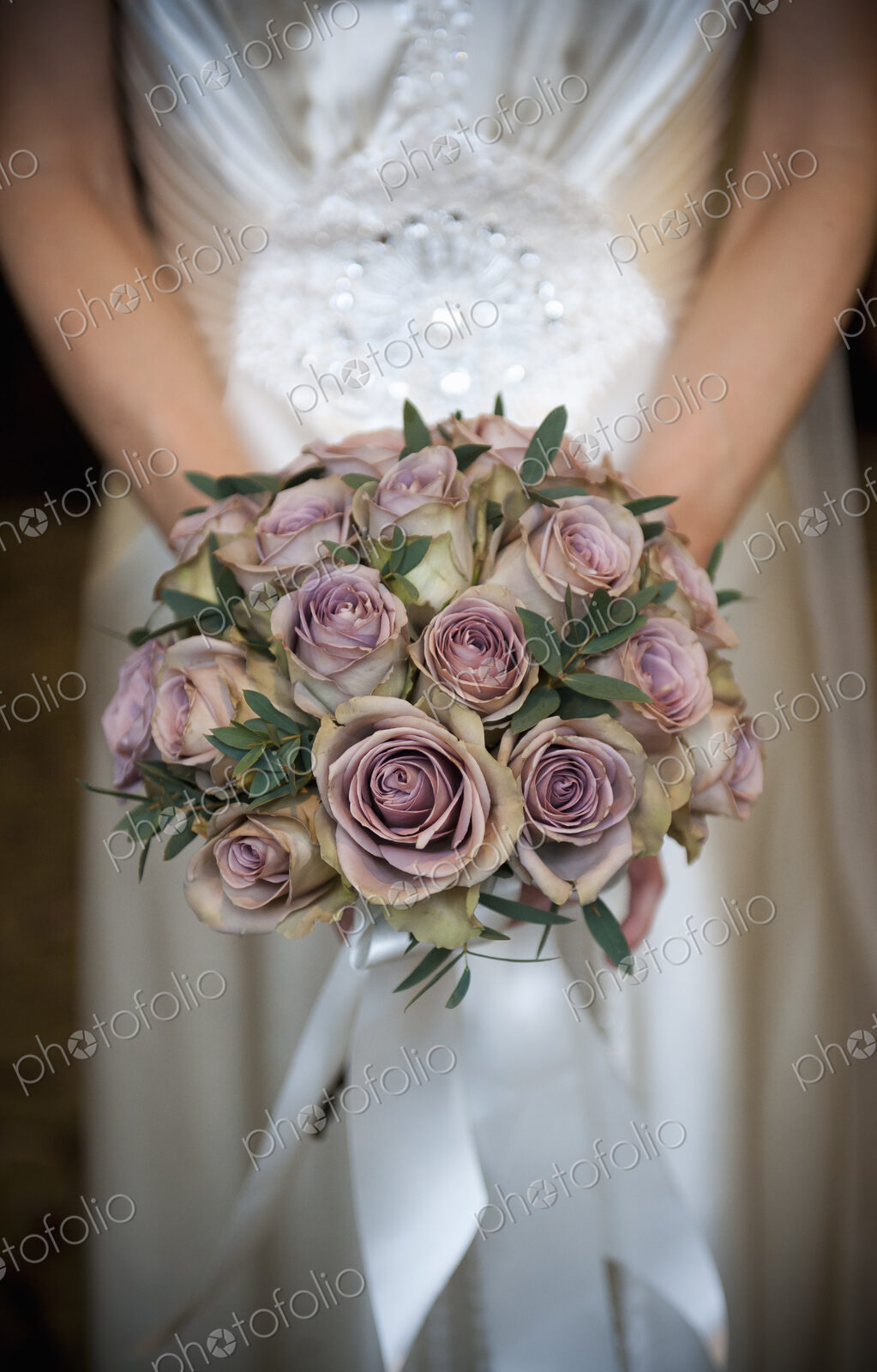 A bride in a white dress, holding a bridal bouquet of pastel coloured roses.