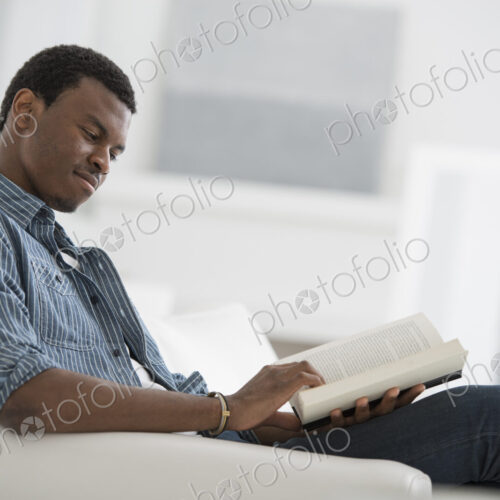 A bright white room interior. A man sitting reading a book.