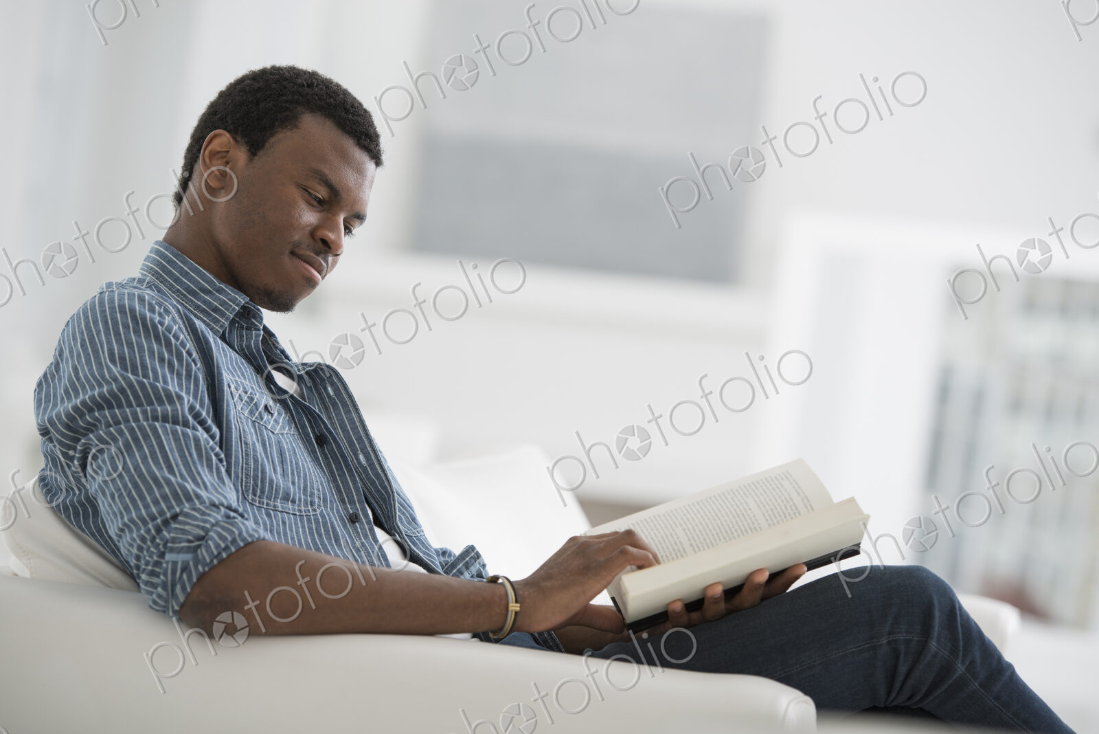 A bright white room interior. A man sitting reading a book.