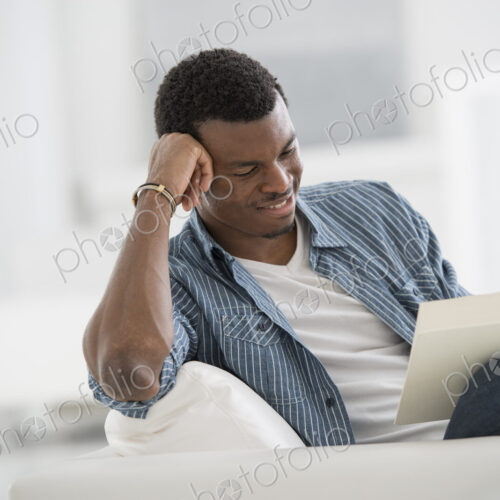 A bright white room interior. A man sitting reading a book.