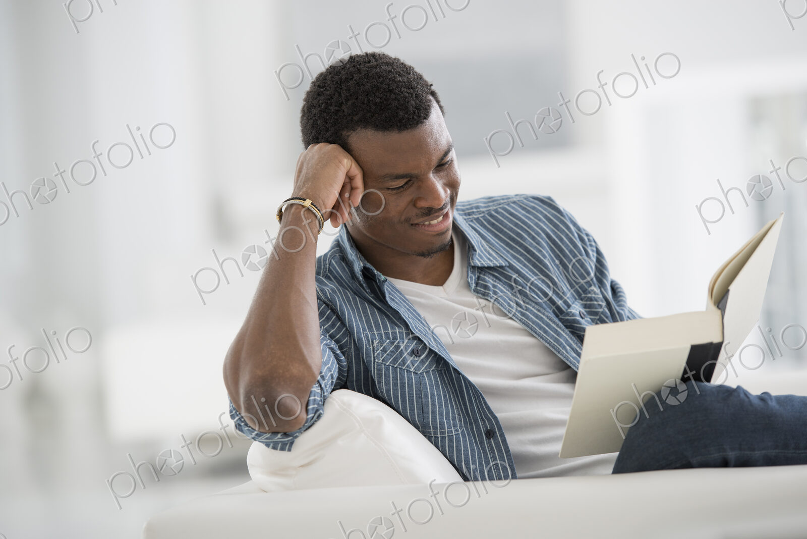 A bright white room interior. A man sitting reading a book.