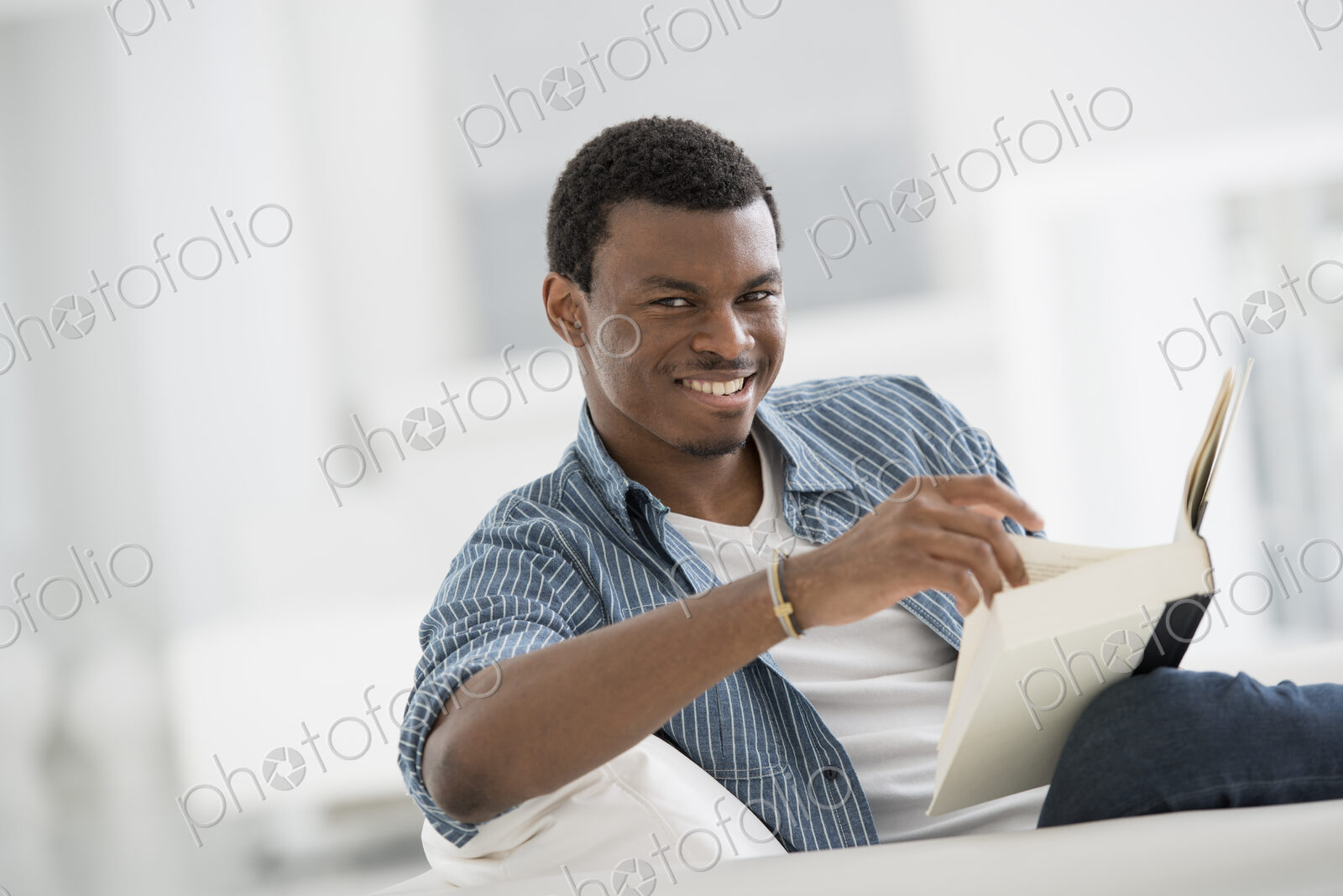 A bright white room interior. A man sitting reading a book.