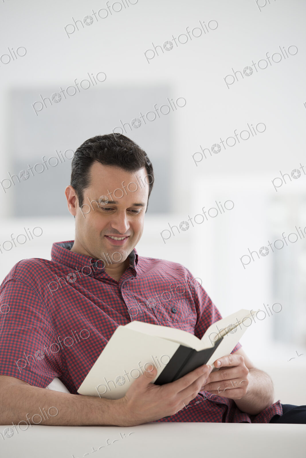 A bright white room interior. A man sitting reading a book.
