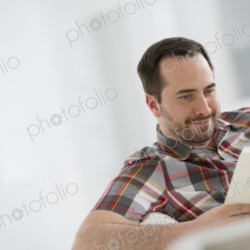 A bright white room interior. A man sitting reading a book.