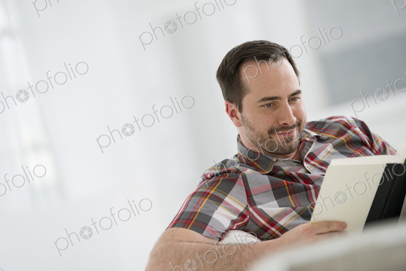 A bright white room interior. A man sitting reading a book.