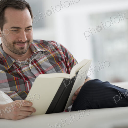 A bright white room interior. A man sitting reading a book.