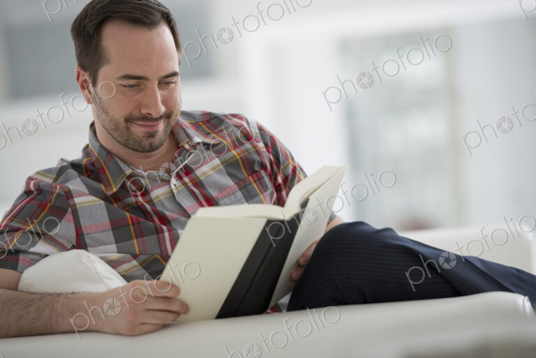 A bright white room interior. A man sitting reading a book.