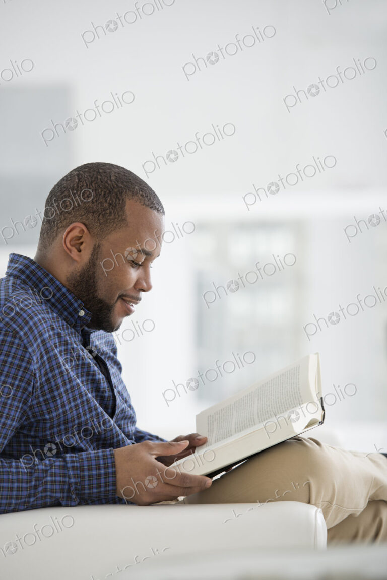 A bright white room interior. A man sitting reading a book.
