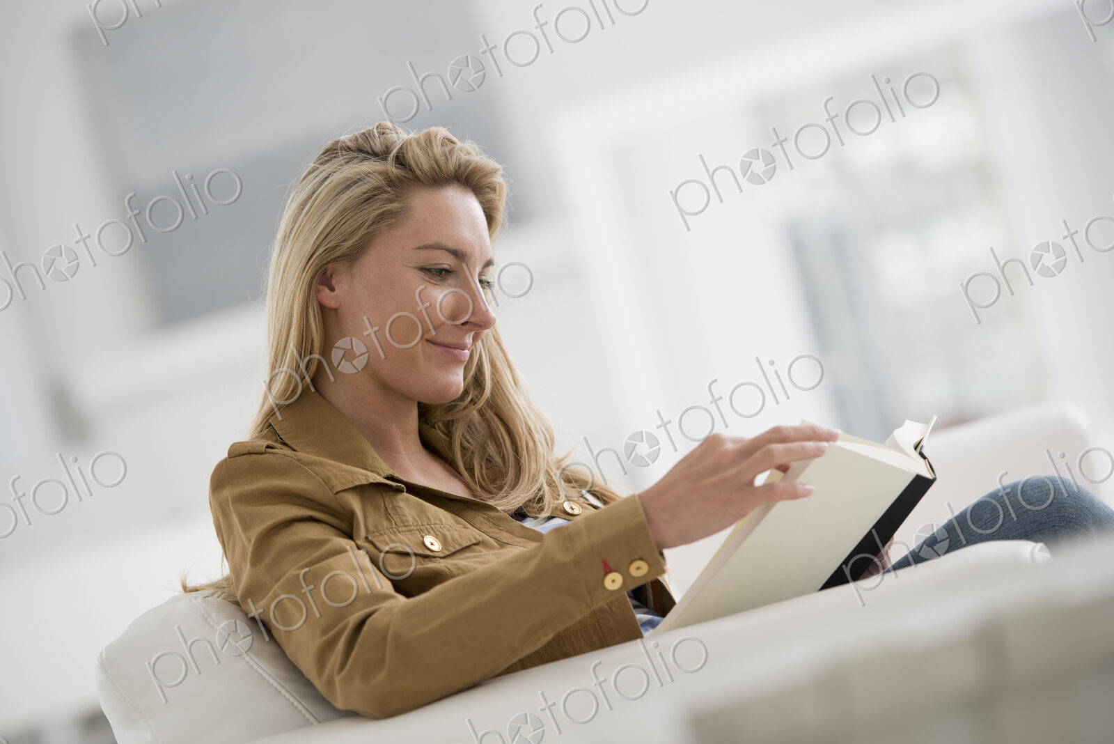 A bright white room interior. A woman sitting reading a book.