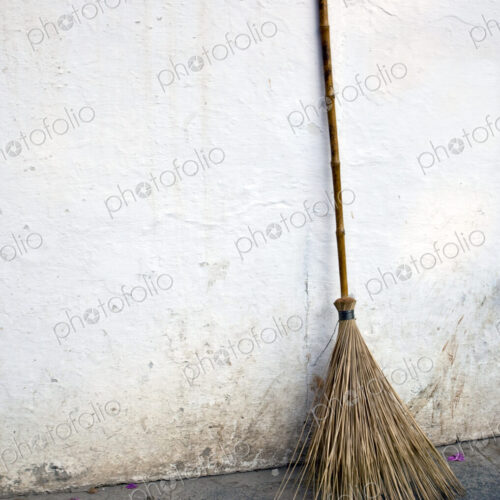 A broom made of twigs with a handle, for sweeping, leaning against a whitewashed wall. A broom made of twigs with a handle, for sweeping, leaning against a whitewashed wall.