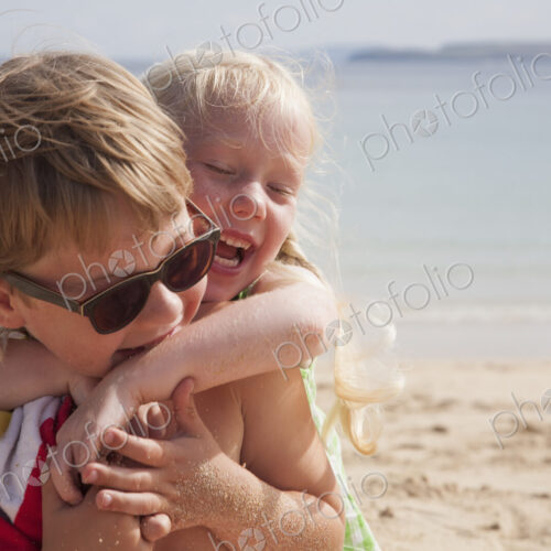 A brother and sister playfighting on the beach. A boy in sunglasses and a younger girl… A brother and sister playfighting on the beach. A boy in sunglasses and a younger girl…
