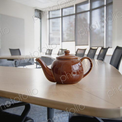 A brown china teapot on boardroom table in empty boardroom.