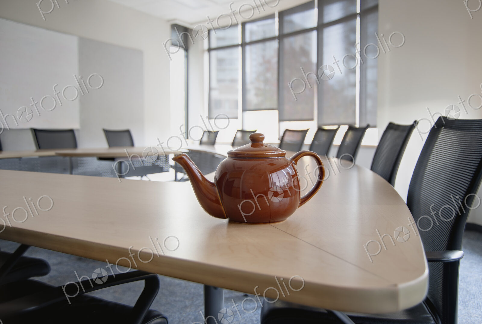A brown china teapot on boardroom table in empty boardroom.