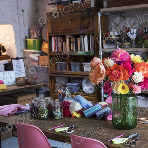 A bunch of colourful handcrafted fabric flowers in a vase on a table in a workshop.