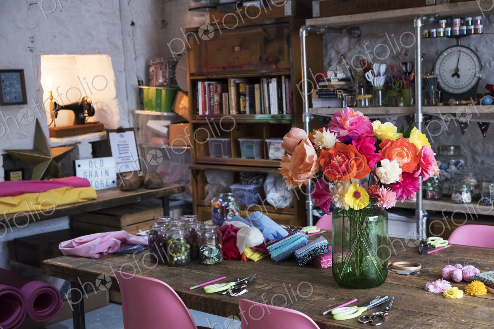 A bunch of colourful handcrafted fabric flowers in a vase on a table in a workshop.