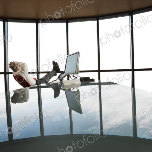 A businessman at his reflective office desk next to a large bank of windows.