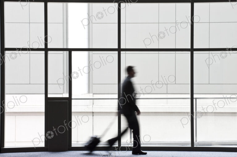 A businessman blurred in silhouette while walking past a large window in a convention…